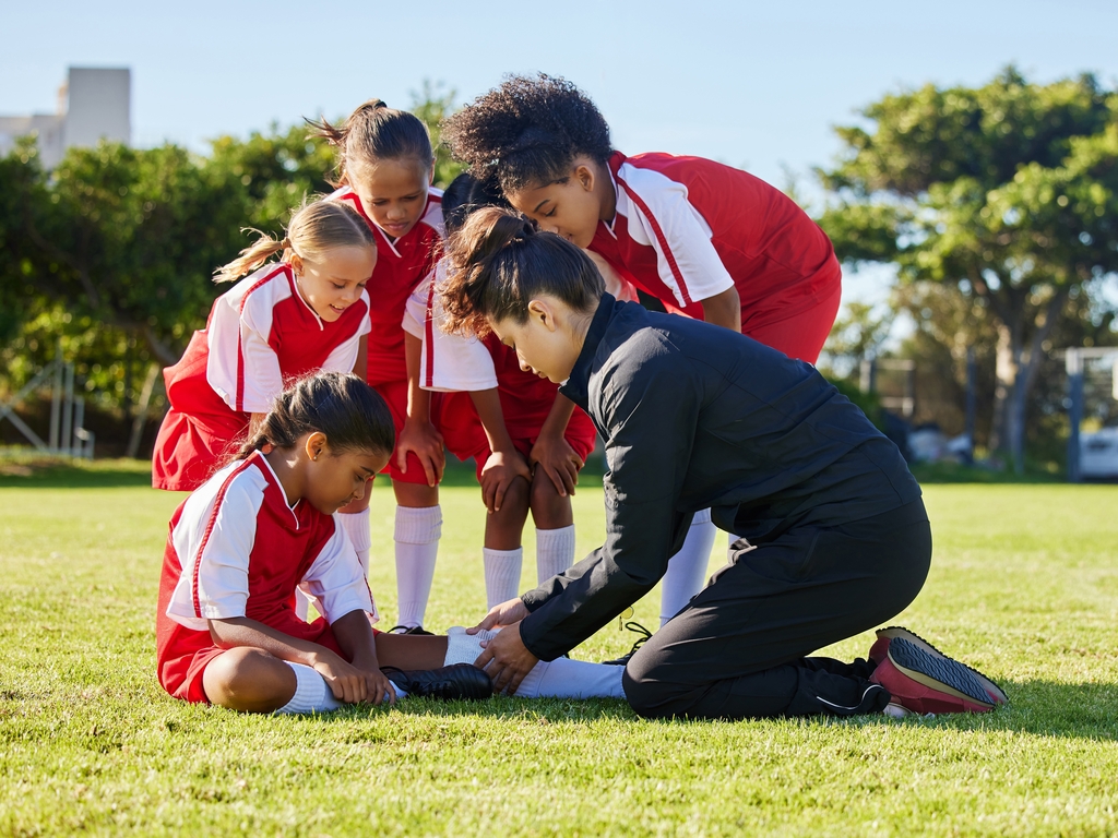 A sports coach performing first aid on an injured child player